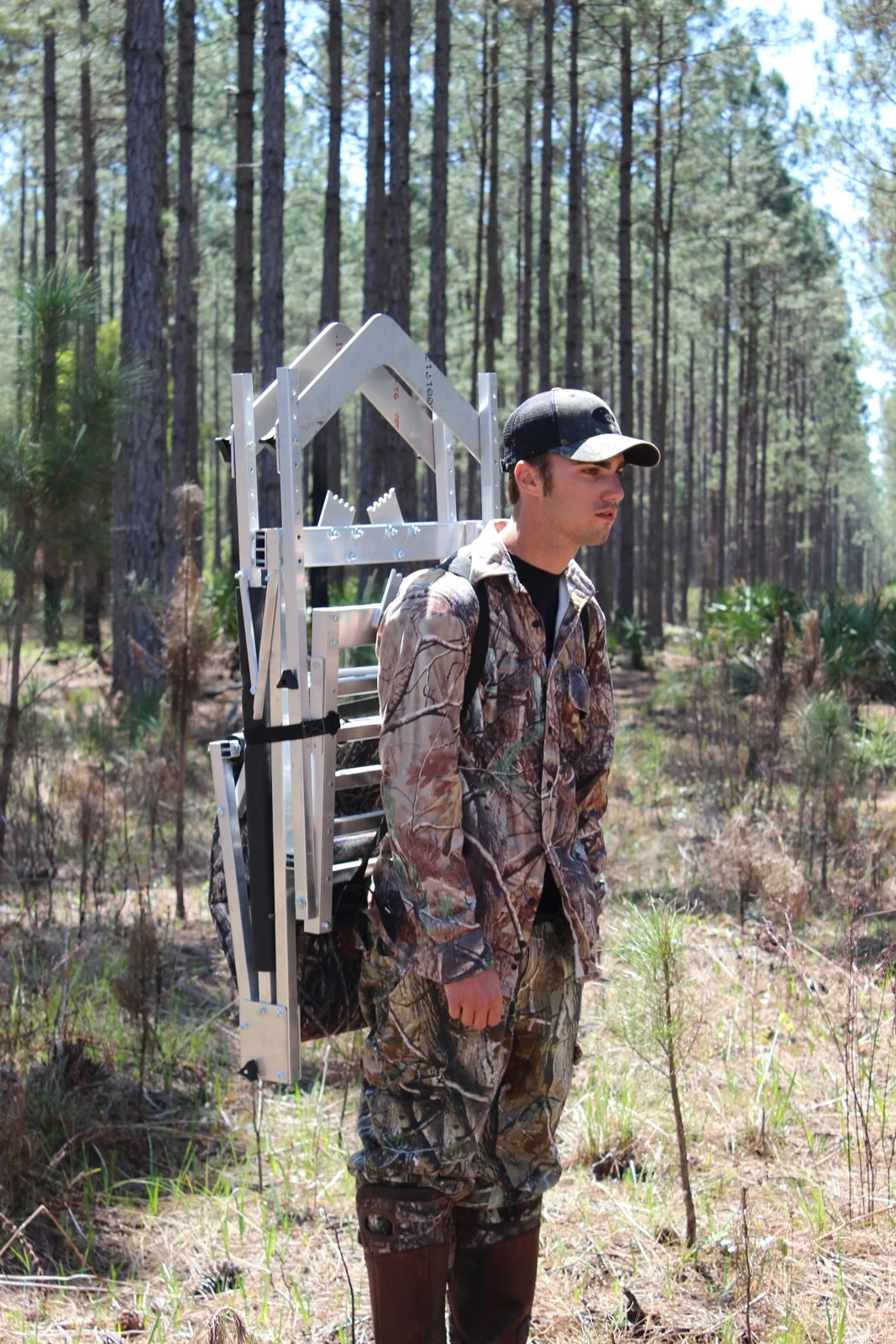 Hunter carrying a folded Gunslinger stand as a backpack through pine woods